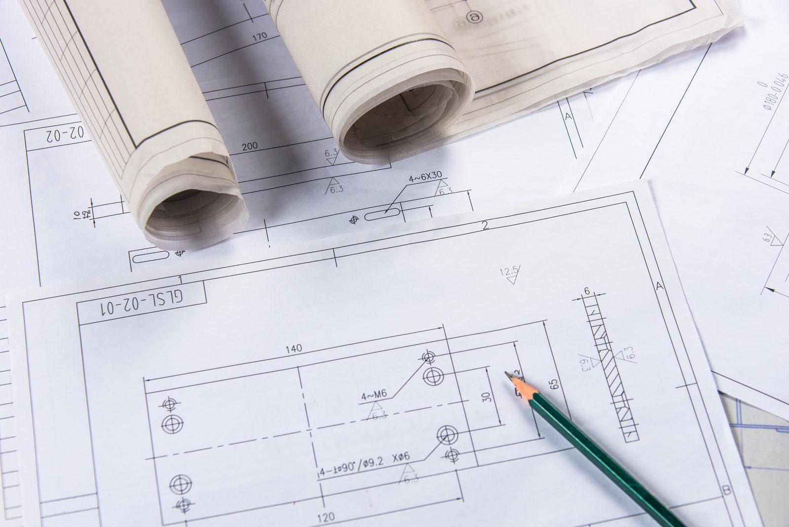Close-up of a dimensioned shop drawing detail with rolled drawing sheets and a pencil