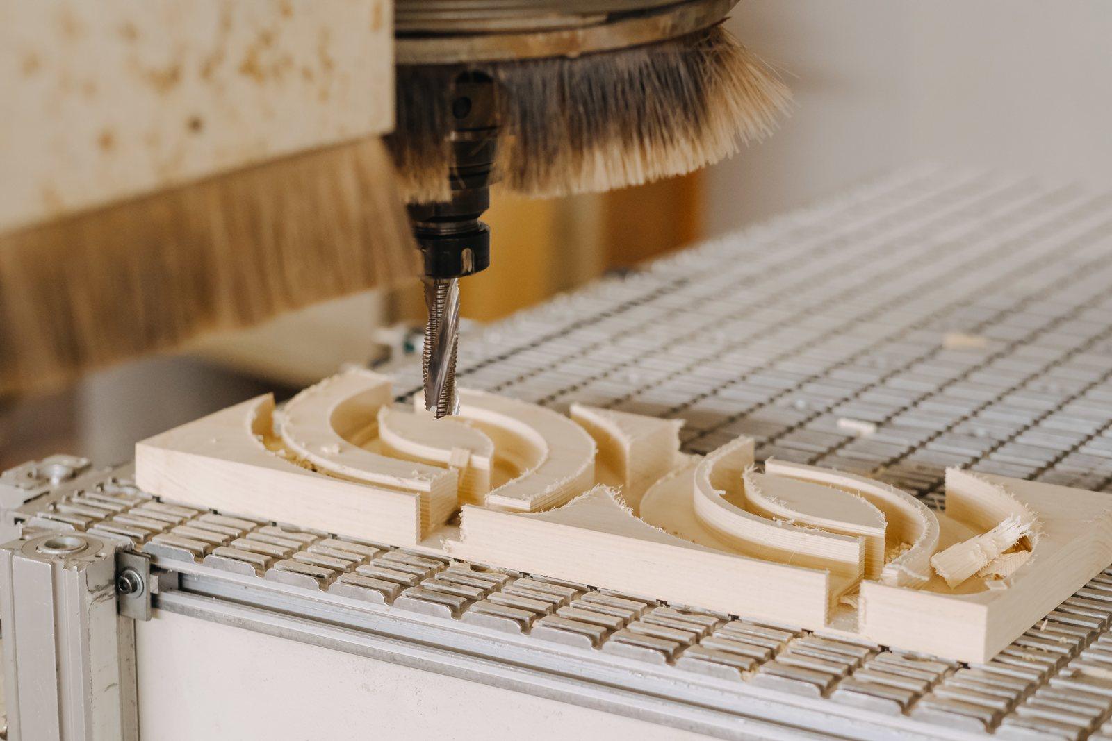 CNC bit carving curved recesses into a wood plank, close up