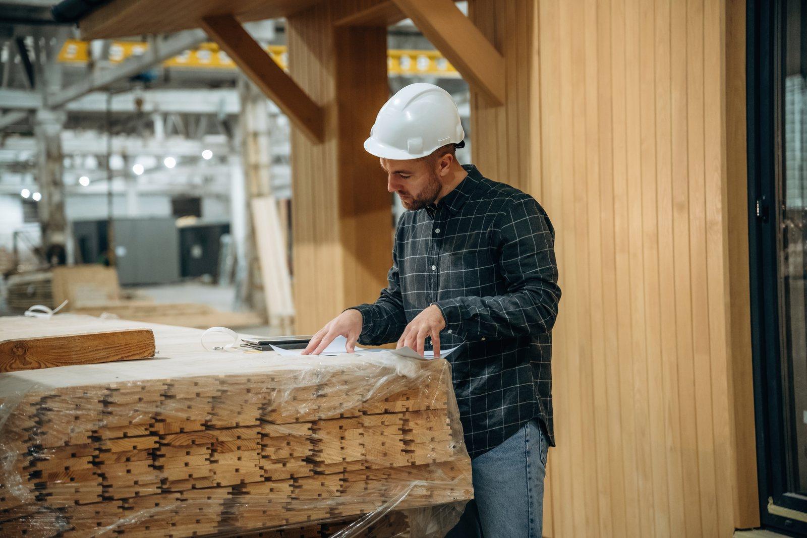 Worker in a hard hat unwrapping bundled millwork panels on a construction site