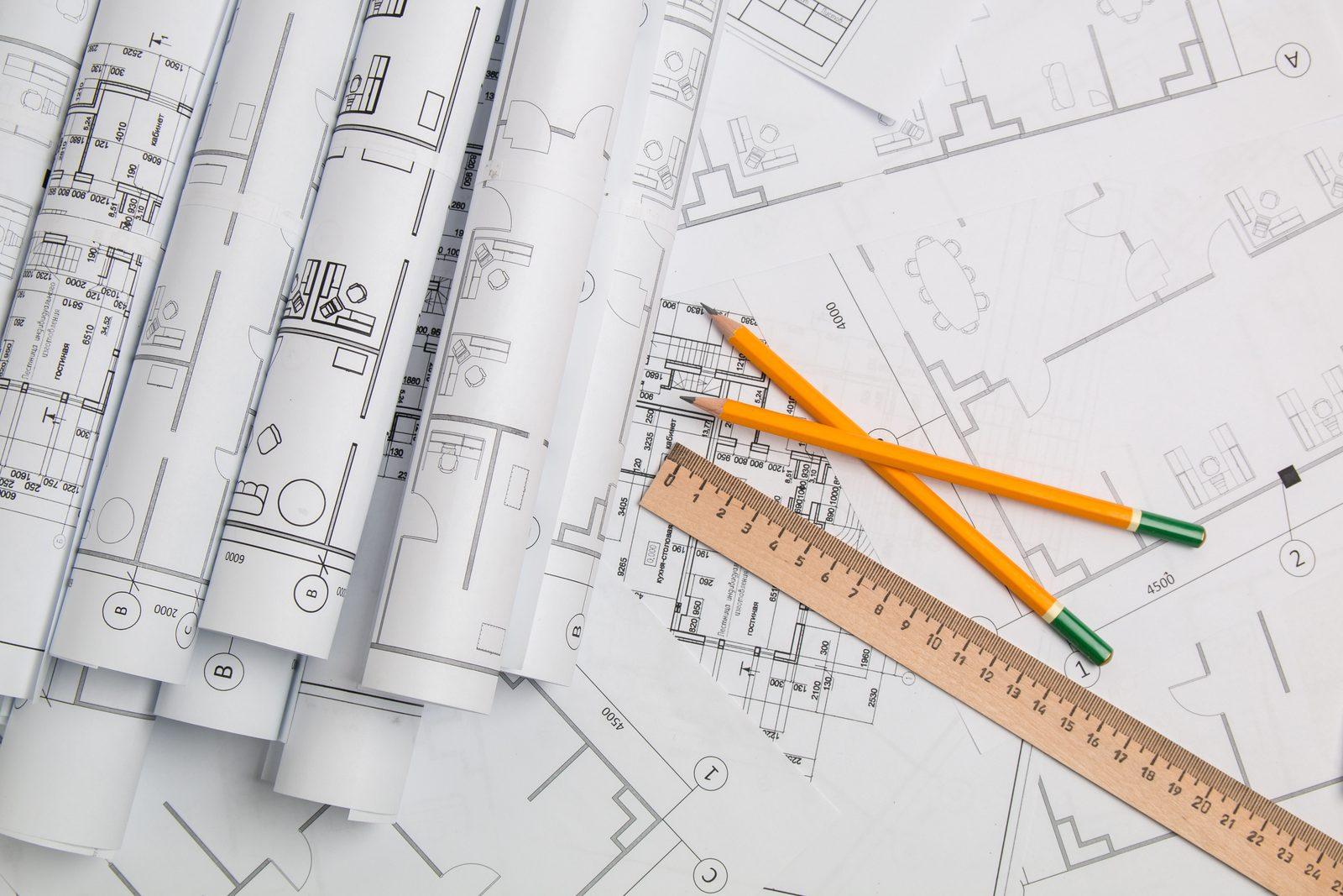 Rolled floor plan drawings with pencils and a ruler laid across further printed plans