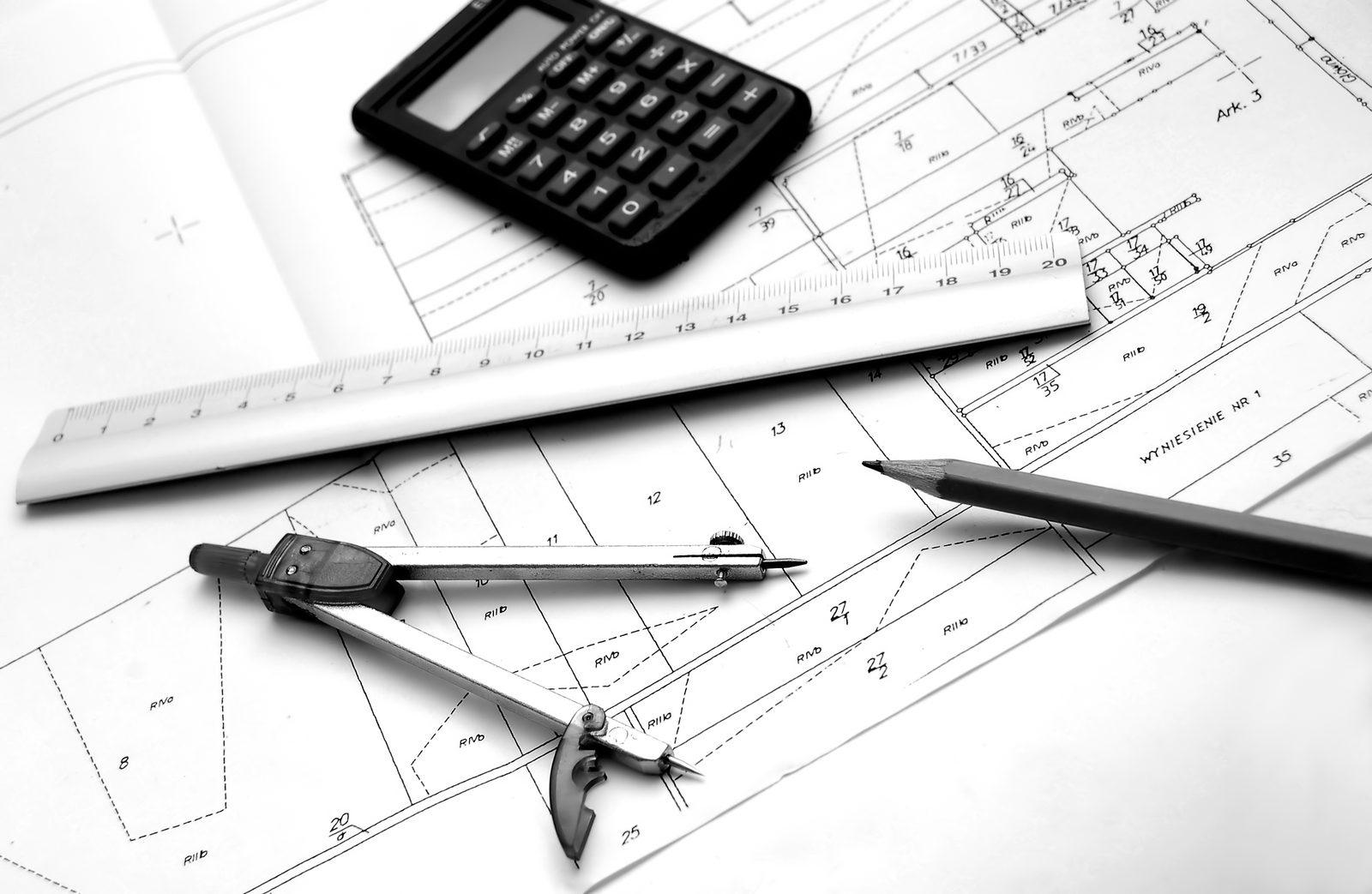 Black and white photo of a calculator, ruler, drafting compass and pencil on a dimensioned drawing