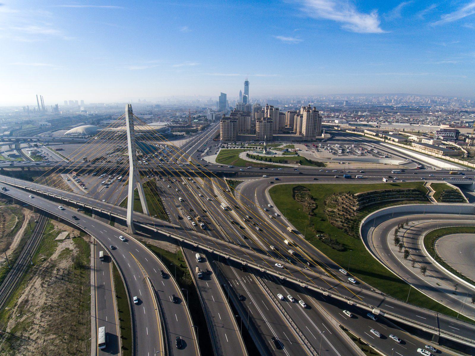 Aerial view of a modern multi-lane highway interchange with a cable-stayed bridge and city skyline