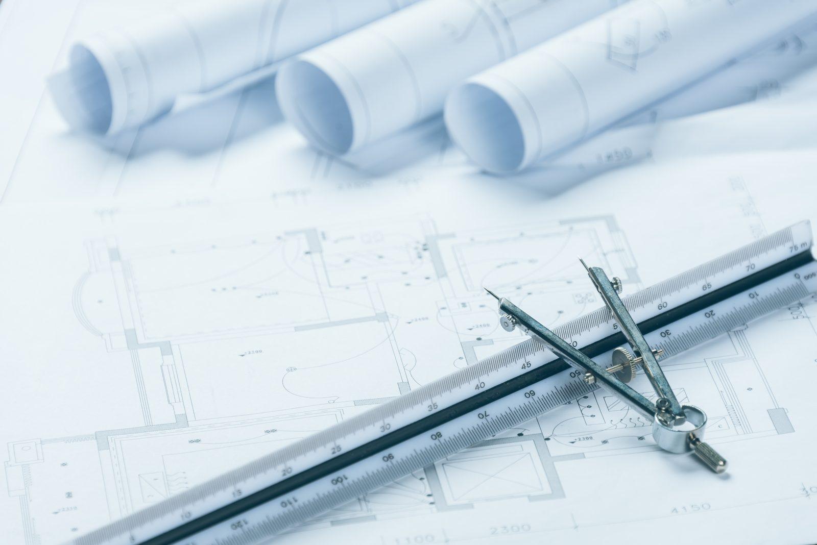 Rolled blueprint drawings, a scale ruler and a drafting compass laid across a printed floor plan