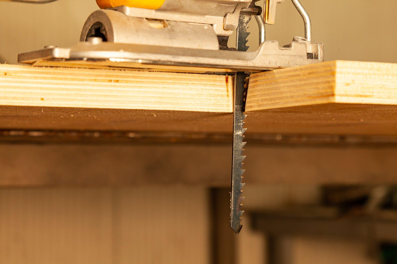 Yellow jigsaw resting on a workbench beside cut sawn wood
