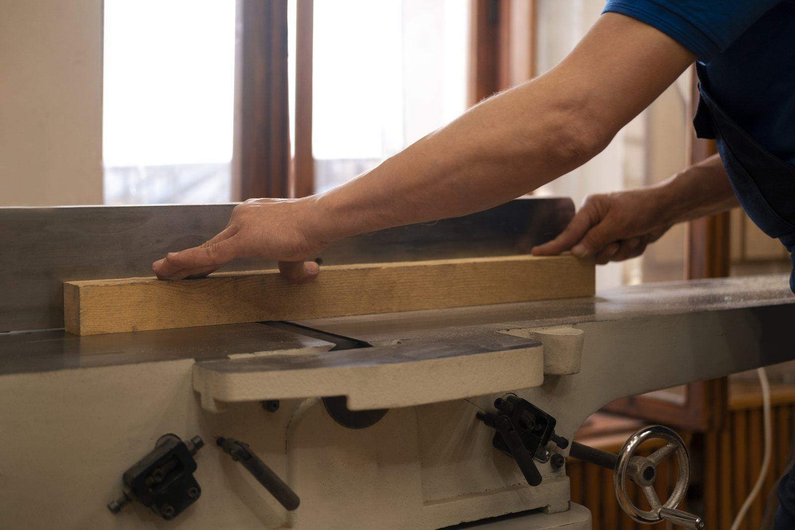Worker guiding a board through a jointer in a wood shop