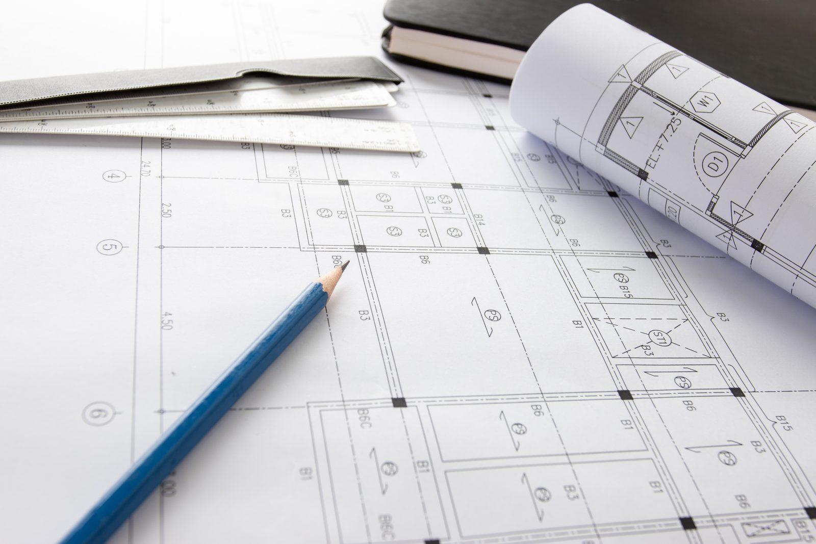 Rolled architectural drawing sheets with a scale ruler, pencil and notebook on a floor plan